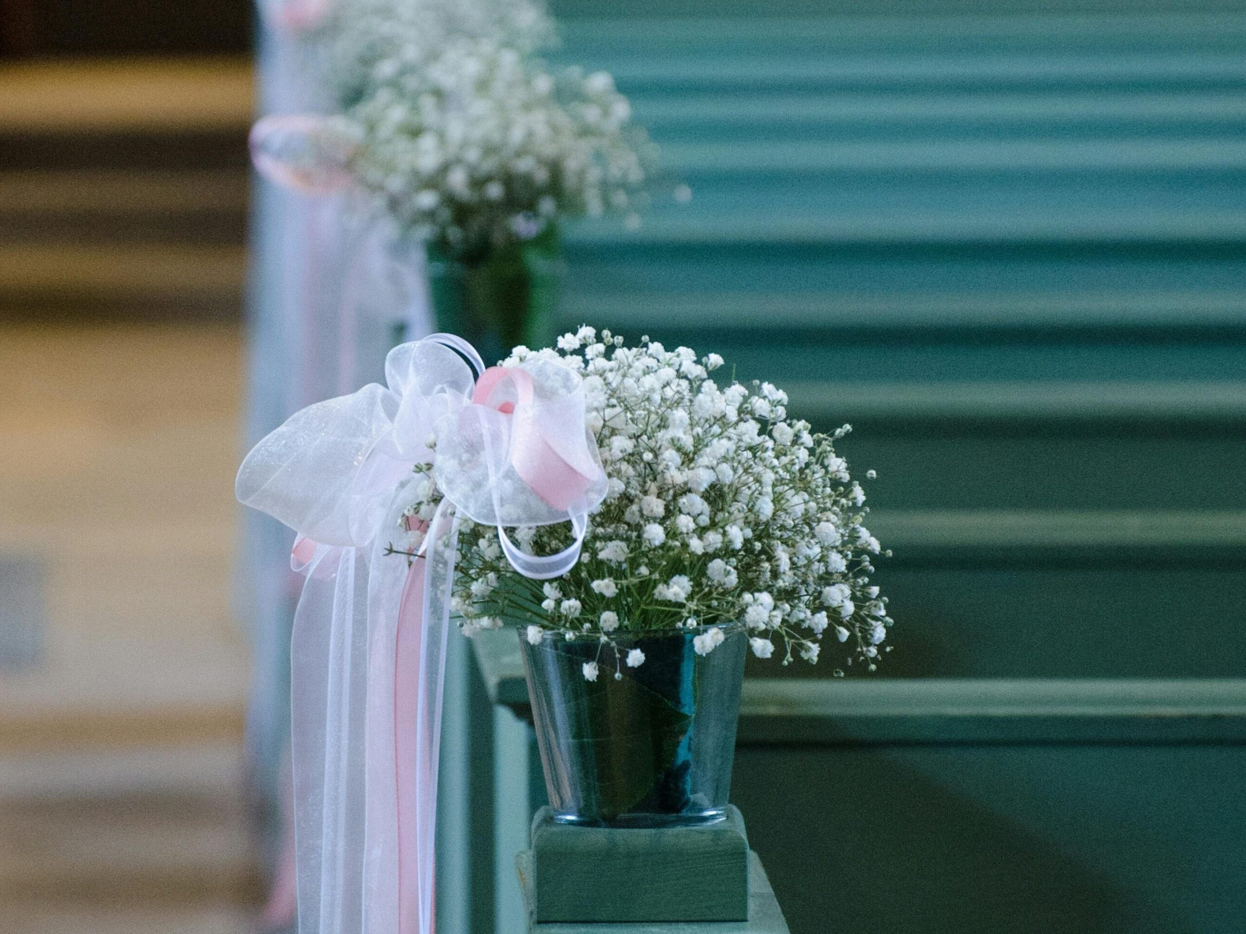 Decoración floral bancos iglesia. Flores blancas sencillas con lazo rosado.