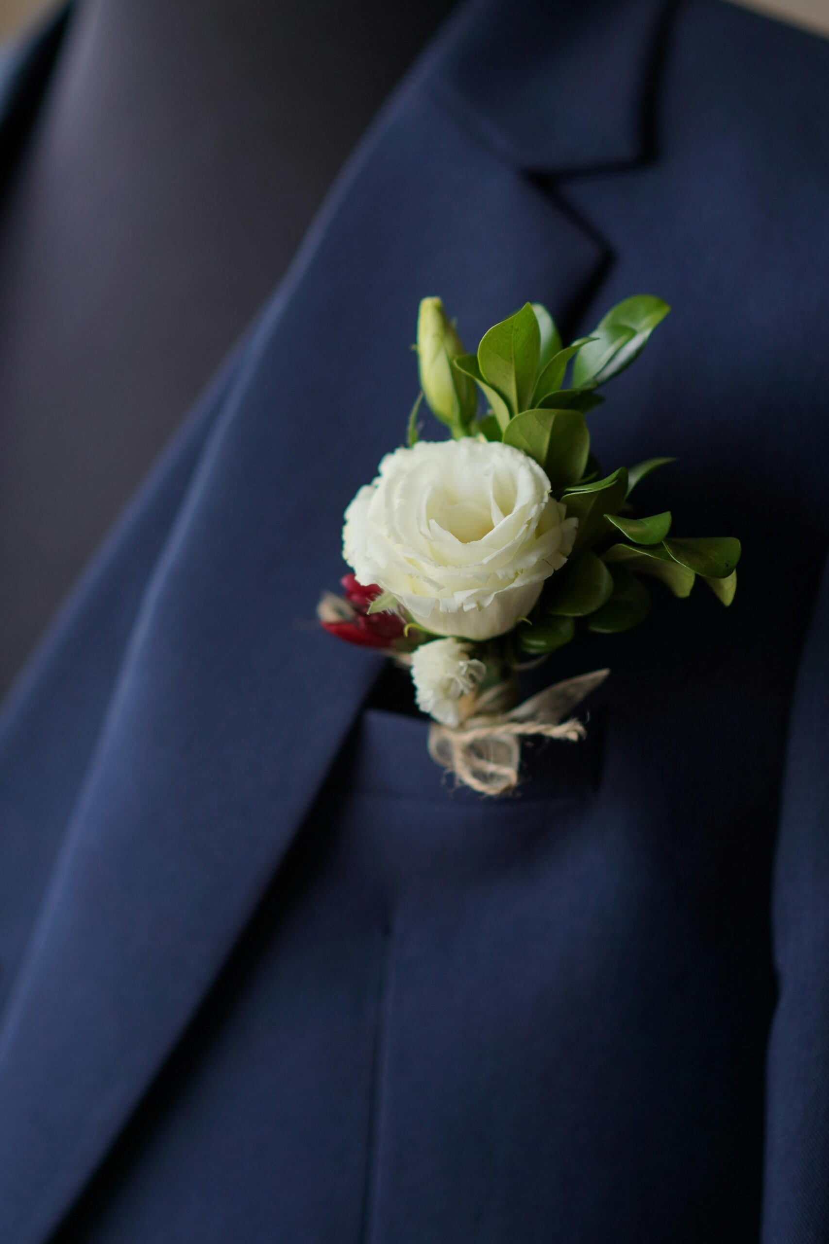 Traje novio azul marino con detalle en bolsillo de rosa blanca y follaje de adorno