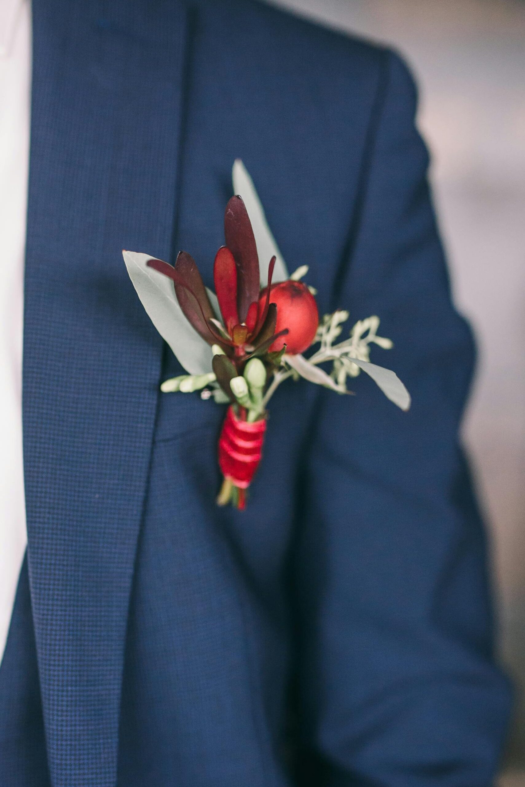 Novio con traje azul marino y detalle de flores rojas y follaje en el bolsillo