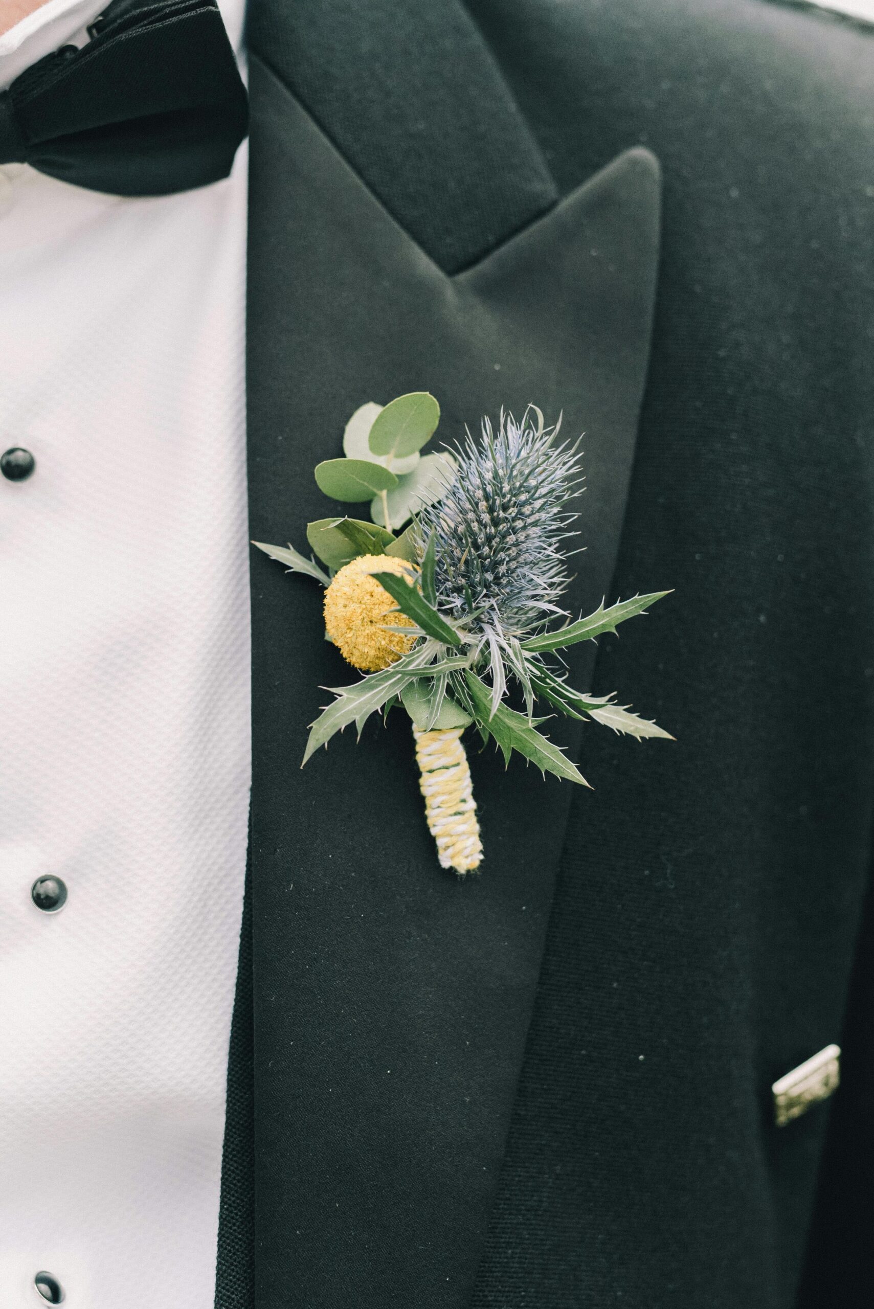 boutonniere de follaje verde, eucalipto, cardo sobre traje color verde