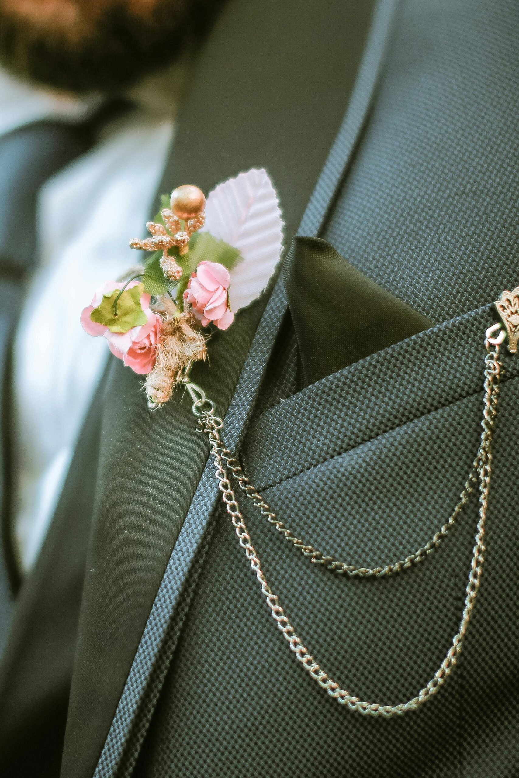 Boutonniere de flores rosas y detalle de hoja blanca con colgante en oro